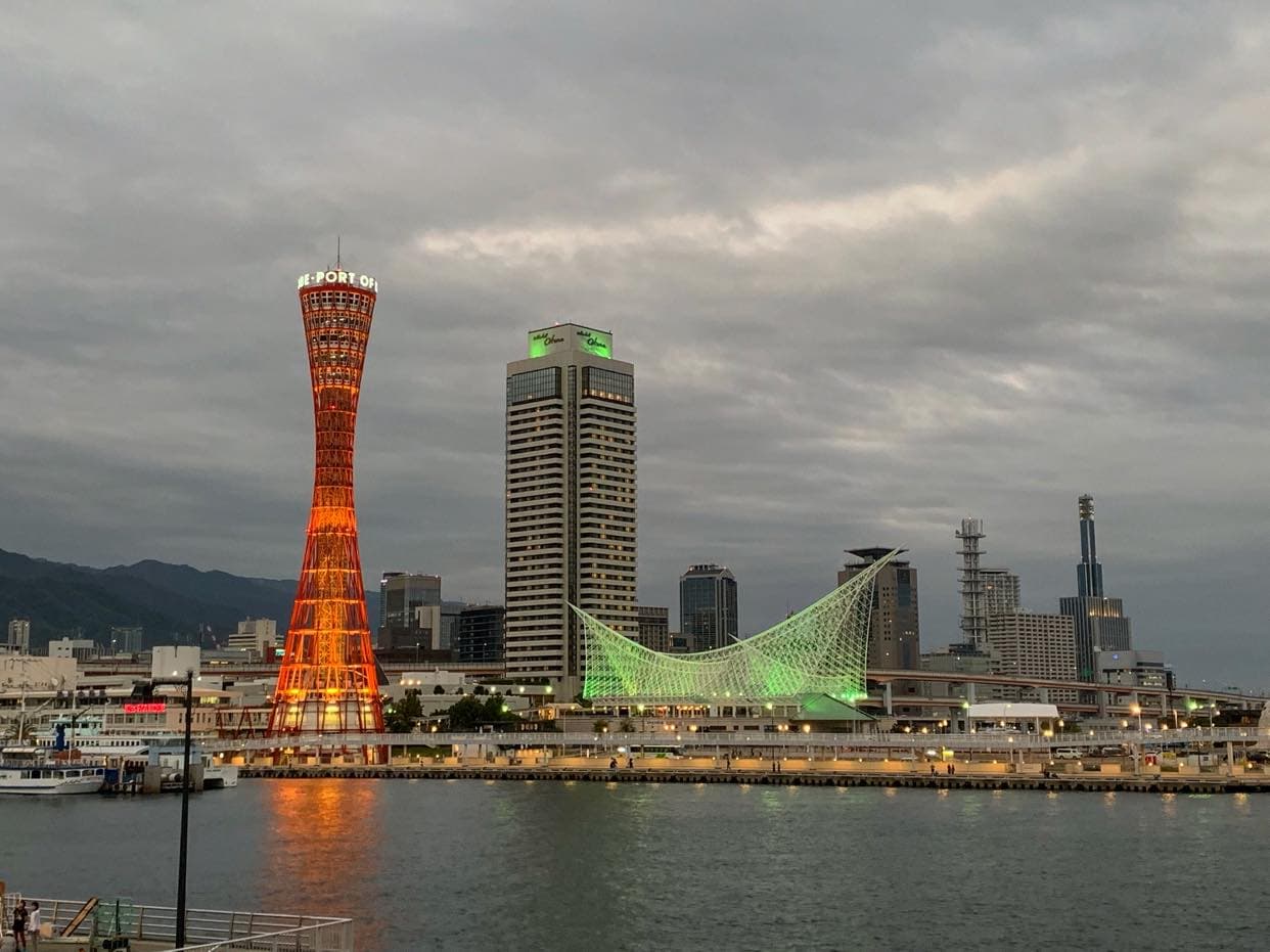 De rode Kobe Port Tower en het verlichte Maritiem Museum boven de haven in de avondschemering, gezien vanaf het water