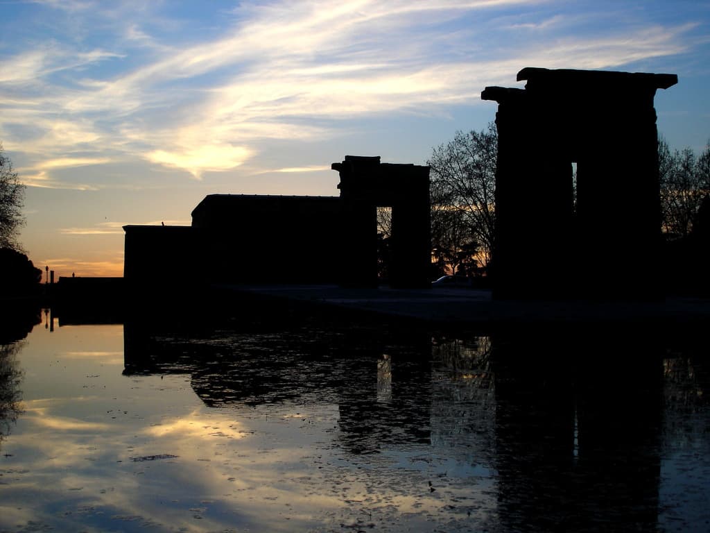 Het Templo de Debod als silhouet tegen de ondergaande zon, weerspiegeld in het water