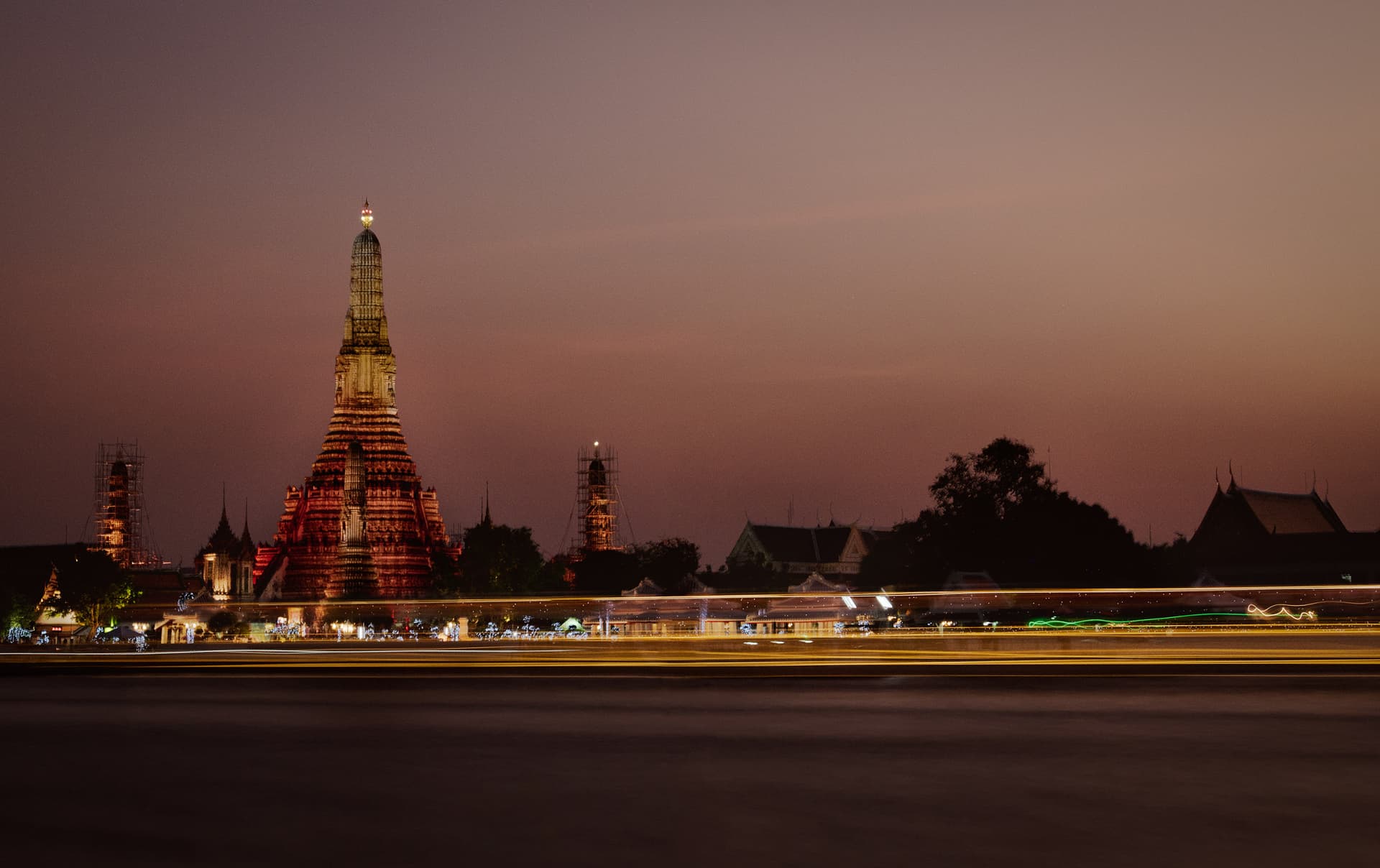 Wat Arun verlicht aan de overkant van de Chao Phraya in Bangkok bij het invallen van de avond