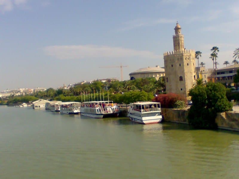 Kleine rondvaartbootjes aan de oever van de Guadalquivir in Sevilla, bij een oude wachttoren